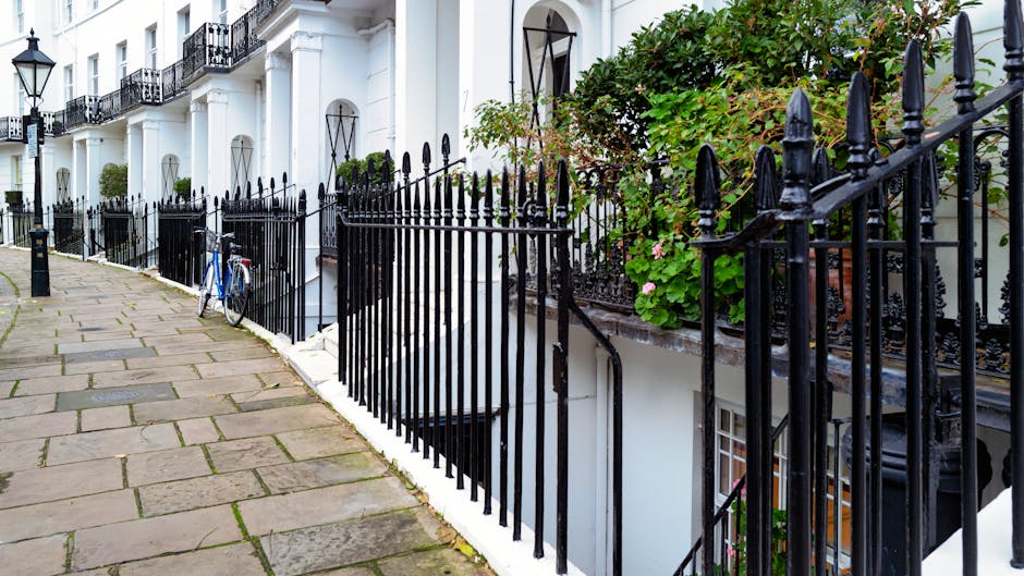 Exterior view of residential homes on Berkeley Square in Mayfair, showing a row of Georgian-style buildings with brick facades and white decorative trim. The buildings feature small balconies with ornate wrought-iron railings, potted plants, and a traditional black street lamp on the sidewalk. The scene is well-lit with natural daylight, highlighting the clean, well-maintained surfaces of the building exteriors. Cleanermayfair.org.uk specializes in surface cleaning, deep cleaning, and sanitisation for such historic homes, ensuring their features remain pristine and hygienic.