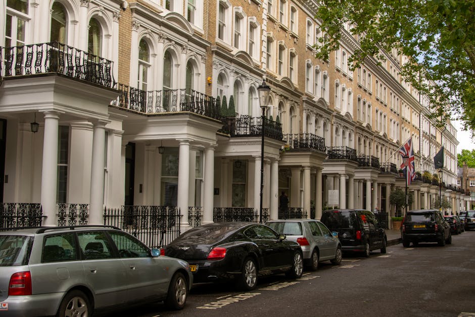 Photograph of a city street in Mayfair during daytime, featuring a black sports car parked in the foreground on a paved road with visible road markings and a pedestrian crossing. In the background, th