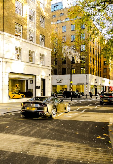 A quiet street in Mayfair during daytime, lined with historic multi-storey buildings featuring brick and stone facades, large windows, and decorative elements such as lantern-style lamps and Union Jac